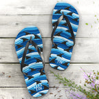 Blue shark-patterned flip-flops on a wooden surface with flowers.