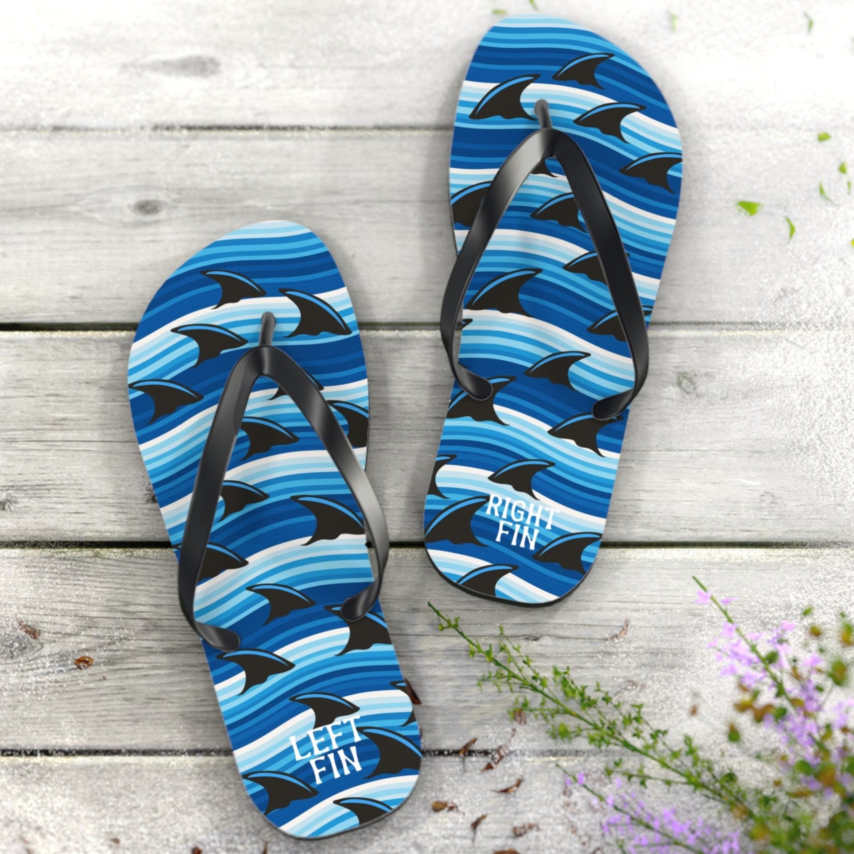 Blue shark-patterned flip-flops on a wooden surface with flowers.
