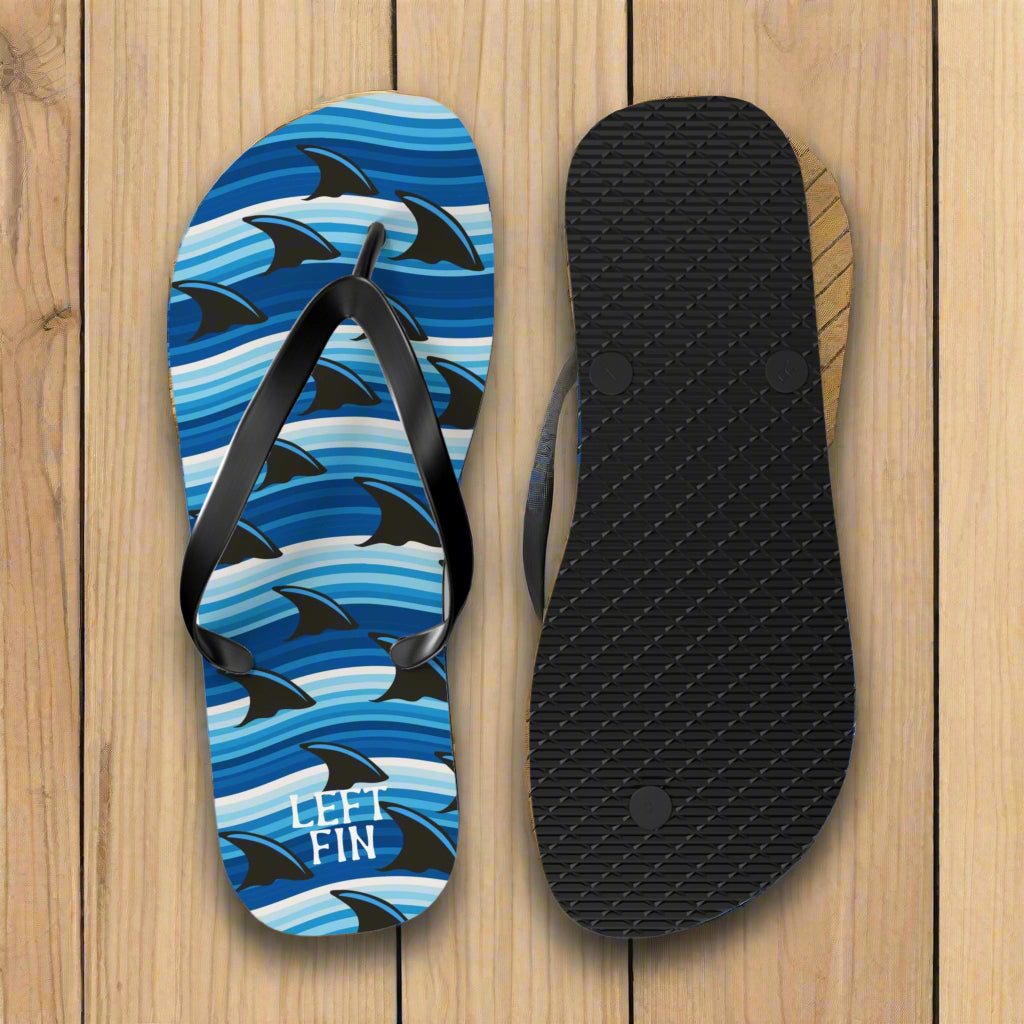 Flip-flop with shark pattern and 'LEFT FIN' text on a nautical wood background
