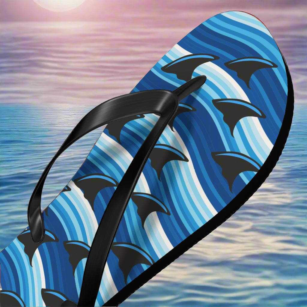 Flip-flop with blue wave and black shark fin pattern on a blue ocean background