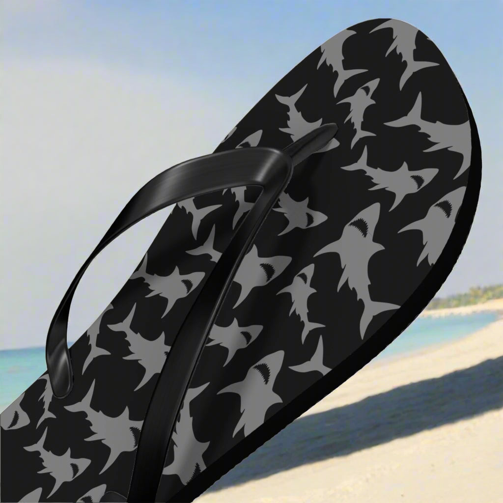 Black flip-flop with shark pattern on a beach background