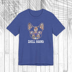 A heather blue short-sleeve t-shirt featuring a colorful seashell graphic of a French Bulldog with the text 'SHELL HOUND' printed below it, displayed flat against a white wood plank background.