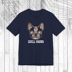 A dark navy short-sleeve t-shirt with a graphic of a French Bulldog decorated with a colorful seashell pattern and the text 'SHELL HOUND' printed below in white, displayed on a white wood plank background.