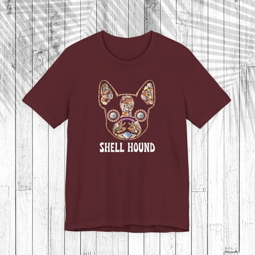 A dark brown short-sleeve t-shirt with a graphic of a French Bulldog decorated with a colorful floral pattern and the text 'SHELL HOUND' printed below in white, displayed on a white wood plank background.