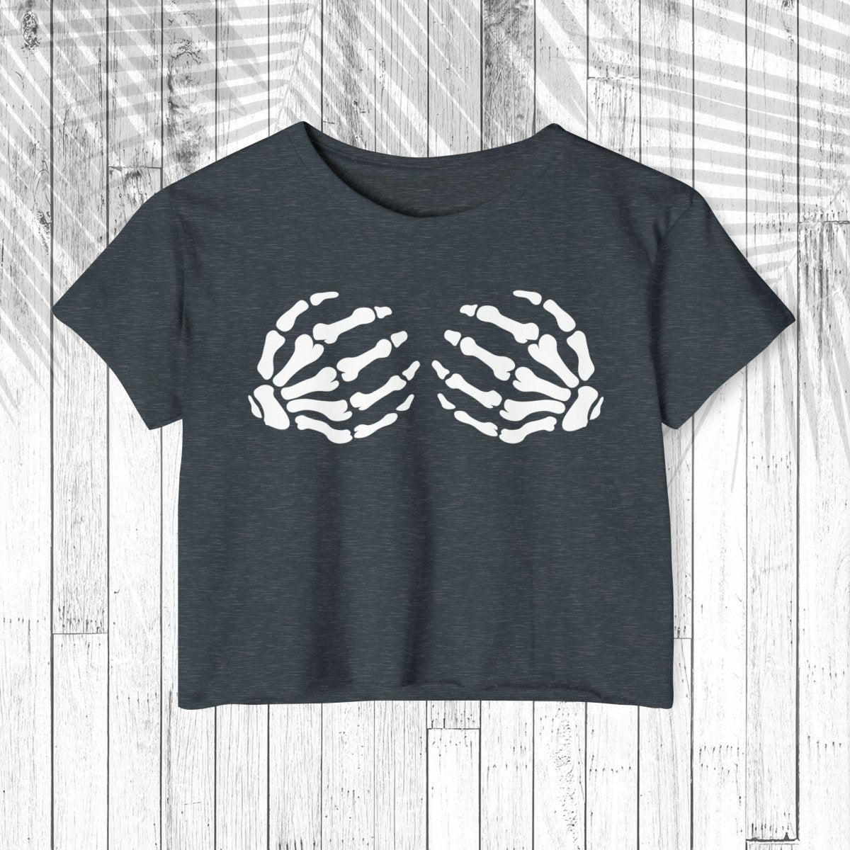 A dark charcoal gray short-sleeve crop top t-shirt featuring a white graphic of two skeletal hands on the chest, displayed flat against a white wood plank background.