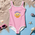 Pink swimsuit with a shell design and 'SHELLO' text on a sandy and blue gradient background.