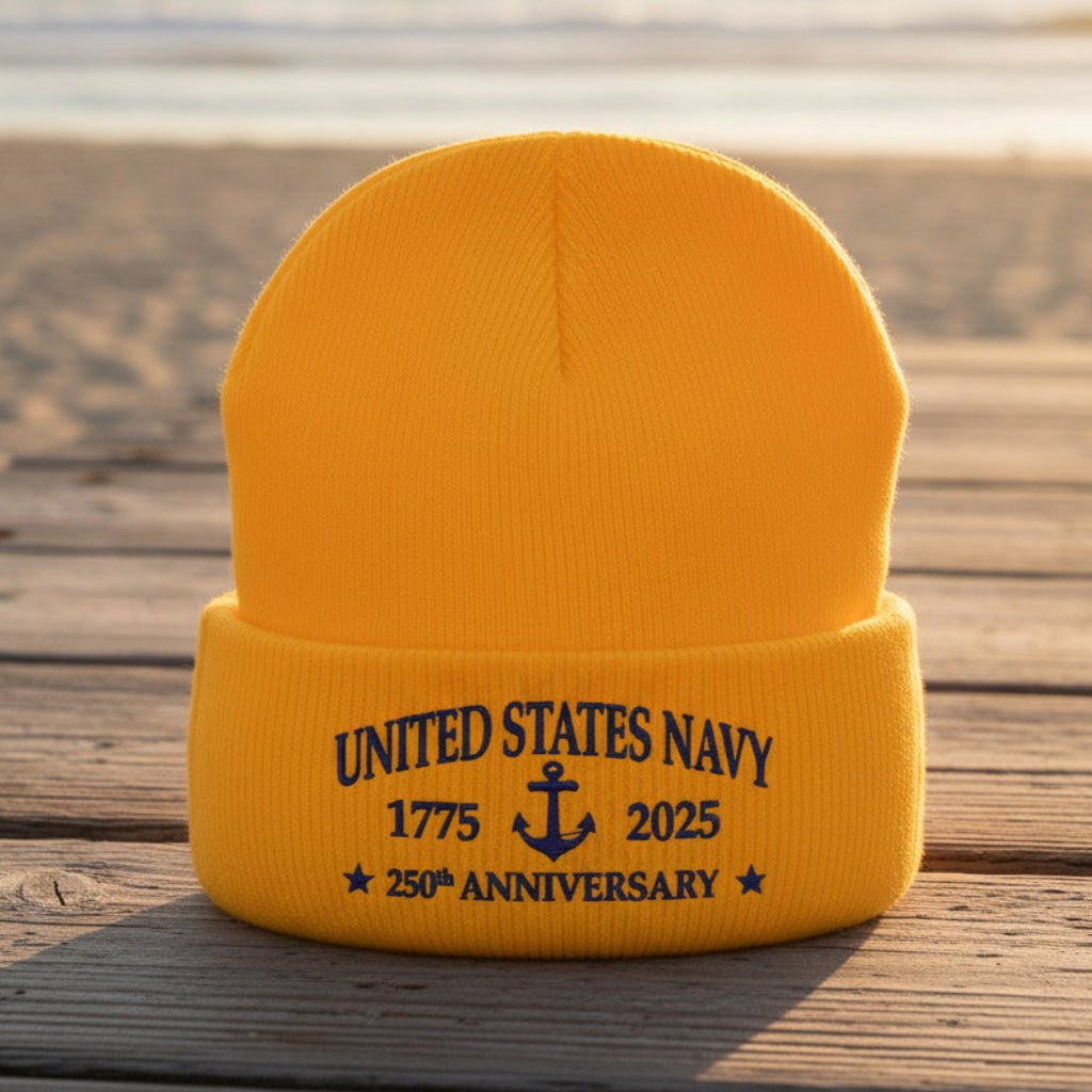 A bright gold cuffed knit beanie hat with navy blue embroidered text reading 'UNITED STATES NAVY 1775 2025 250th ANNIVERSARY' and an anchor graphic on the front cuff.