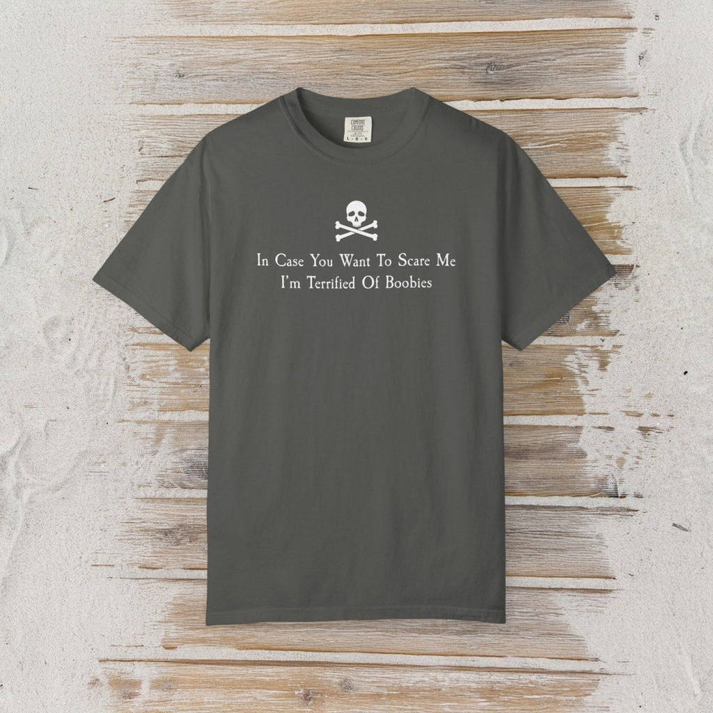 A dark gray crewneck t-shirt with a white skull and crossbones graphic and the text 'In Case You Want To Scare Me I'm Terrified Of Boobies' printed on the chest, displayed flat against a rustic light wood plank background.