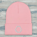 A light pink ribbed knit beanie hat with a folded cuff and a small white embroidered shark jaw embroidery on the front, shown against a rustic wood background