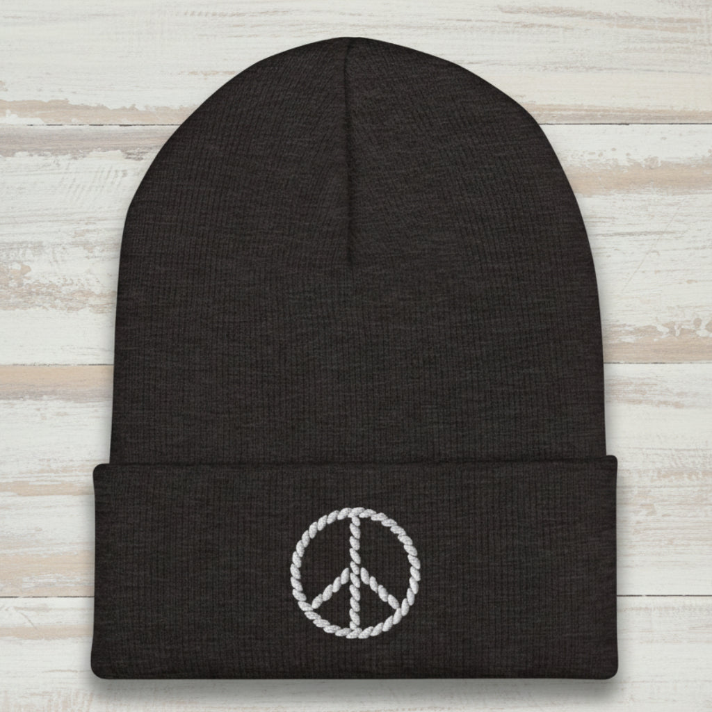 Black beanie with a white peace sign emblem on a rustic wood background