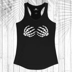 A black racerback tank top with a white skeletal hand graphic printed on the chest, laid flat on a white wood plank background with a palm leaf shadow overlay.