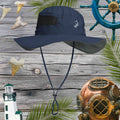 Navy bucket hat with hammerhead shark embroidery on a wooden background with ship wheel, lighthouse, and diving helmet.