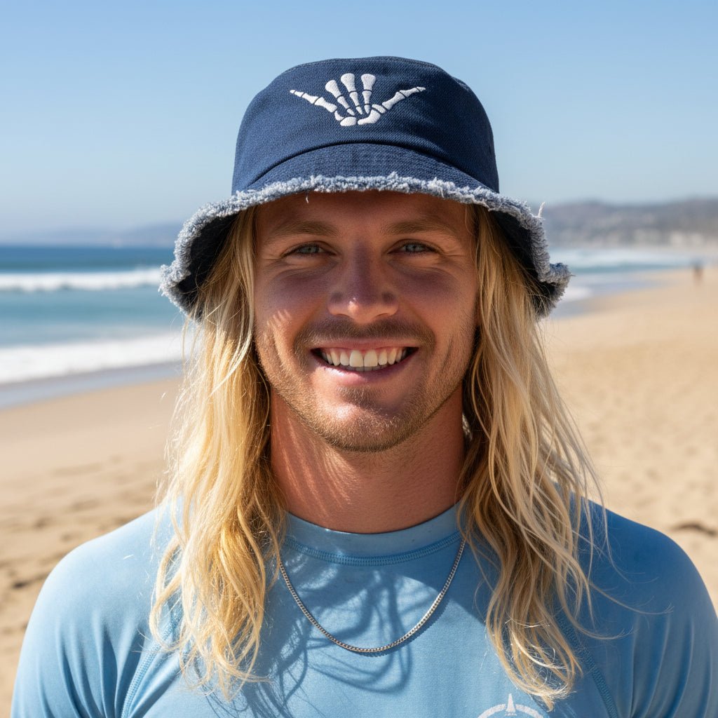 Man wearing a blue bucket hat with a shaka bones logo, smiling against a white background 
