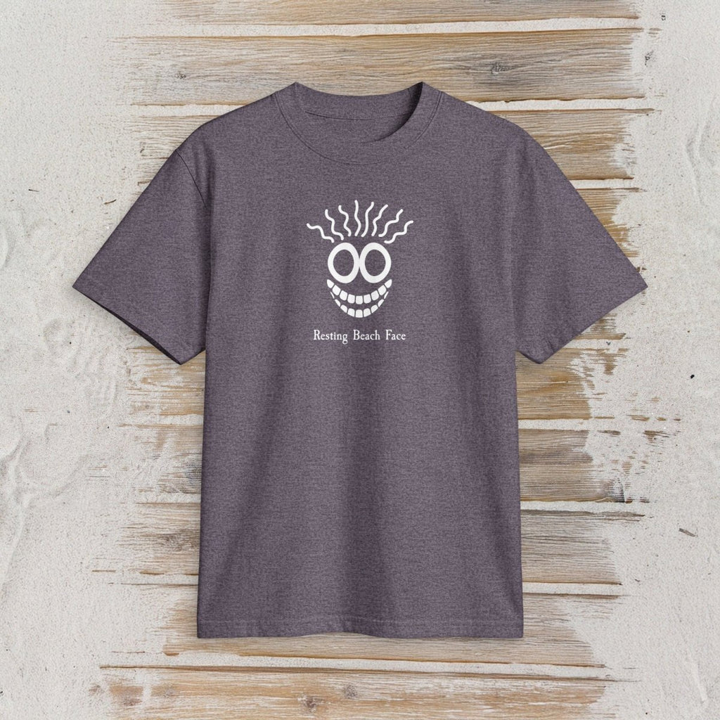 A heather dark purple short-sleeve t-shirt with a white graphic of a smiling face with wavy hair and the text 'Resting Beach Face' printed on the chest, displayed flat on a rustic light wood background.