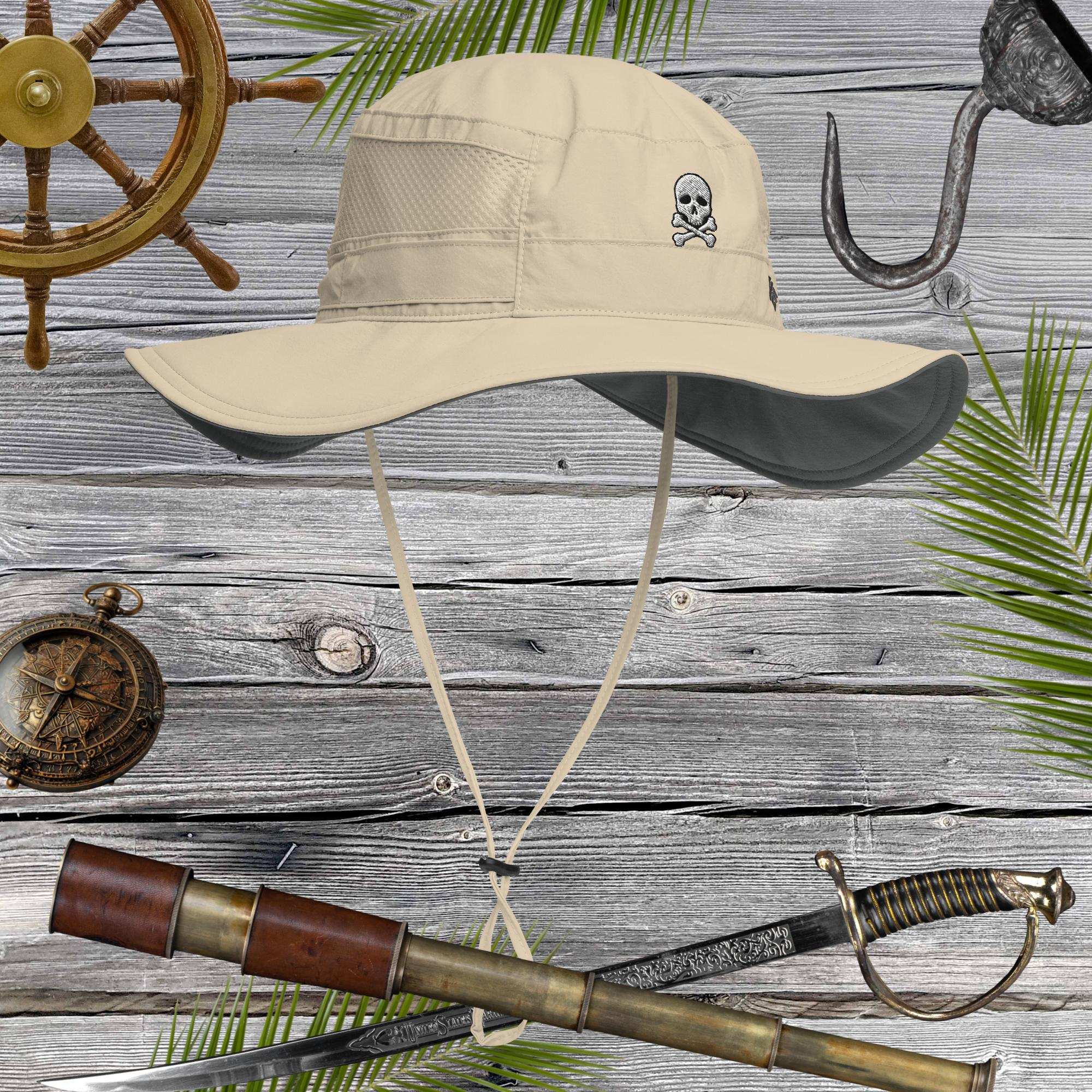 Beige sun hat with embroidered skull and crossbones design on a wooden background with pirate-themed items.