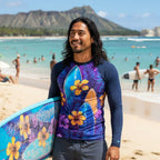 Dude holding a surfboard with a colorful floral pattern on a beach with Diamond Head in the background