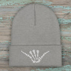 Grey beanie with white shaka skeleton hand embroidery on a rustic wood background