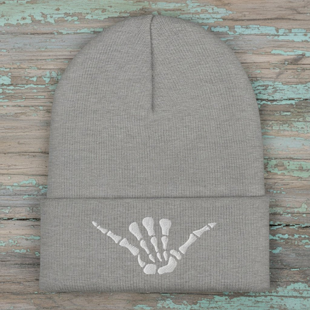 Grey beanie with white shaka skeleton hand embroidery on a rustic wood background