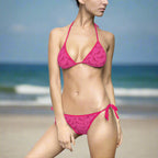 Woman in hot pink bathing suits coverd with a cool shark pattern is standing in the sand with the beach in the background