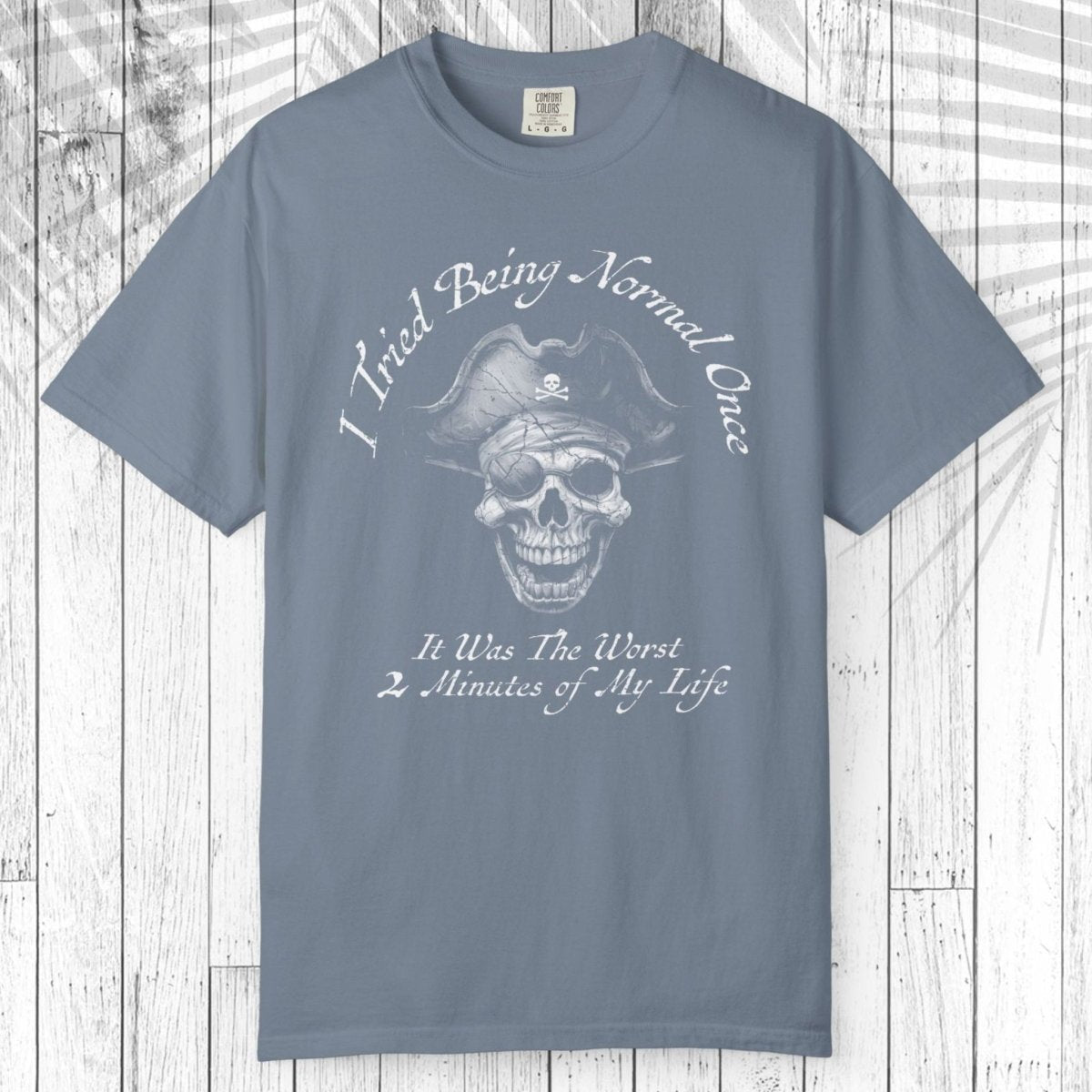 A slate blue short-sleeve t-shirt with a white graphic of a pirate skull and the text 'I Tried Being Normal Once. It Was The Worst 2 Minutes of My Life.