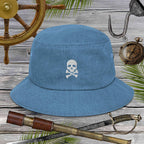 Blue bucket hat with a jolly roger skull and crossbones design on a wooden background with pirate-themed items.