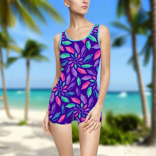 Aqua Trim One Piece Bathing with Junonia seashells in floral pattern worn by a swimwear model standing on the beach looking for junonia.