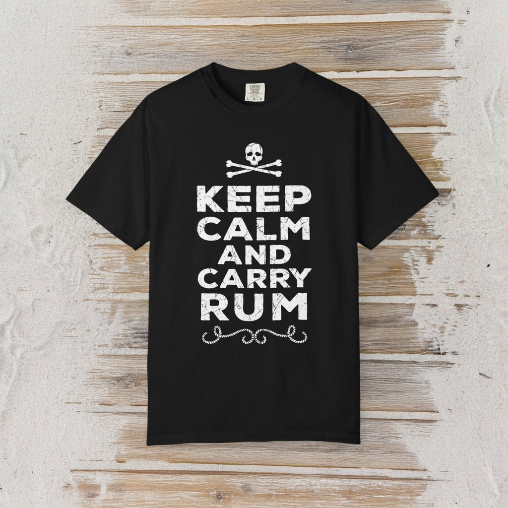 A black short-sleeve crewneck t-shirt with a white graphic print reading 'KEEP CALM AND CARRY RUM' below a skull and crossbones, displayed flat against a rustic light wood plank background.