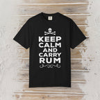 A black short-sleeve crewneck t-shirt with a white graphic print reading 'KEEP CALM AND CARRY RUM' below a skull and crossbones, displayed flat against a rustic light wood plank background.