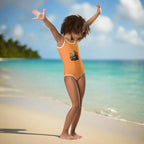 Kid wearing a Girl's One Piece with a Laughing Tiki Bongos print is dancing on the beach in an island paradise
