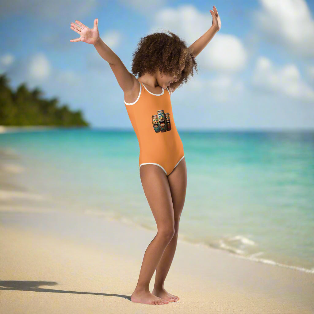 Kid wearing a Girl's One Piece with a Laughing Tiki Bongos print is dancing on the beach in an island paradise