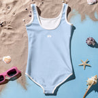 Girl's Sky Blue One Piece Swimsuit back-side lying in sand next to seashells and sunglasses