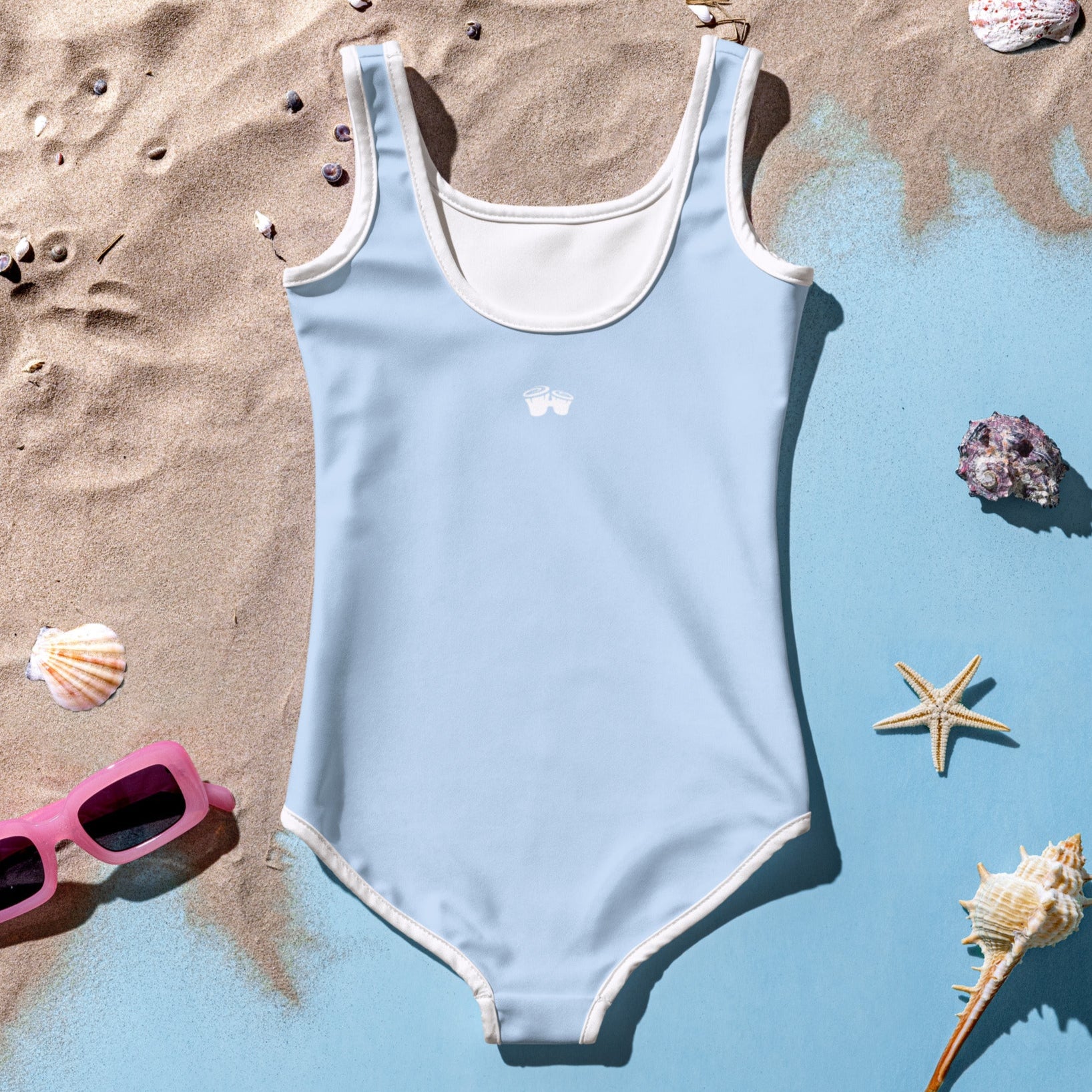 Girl's Sky Blue One Piece Swimsuit back-side lying in sand next to seashells and sunglasses