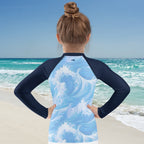 girl wearing a long sleeve rashie with ocean wave design on a beach