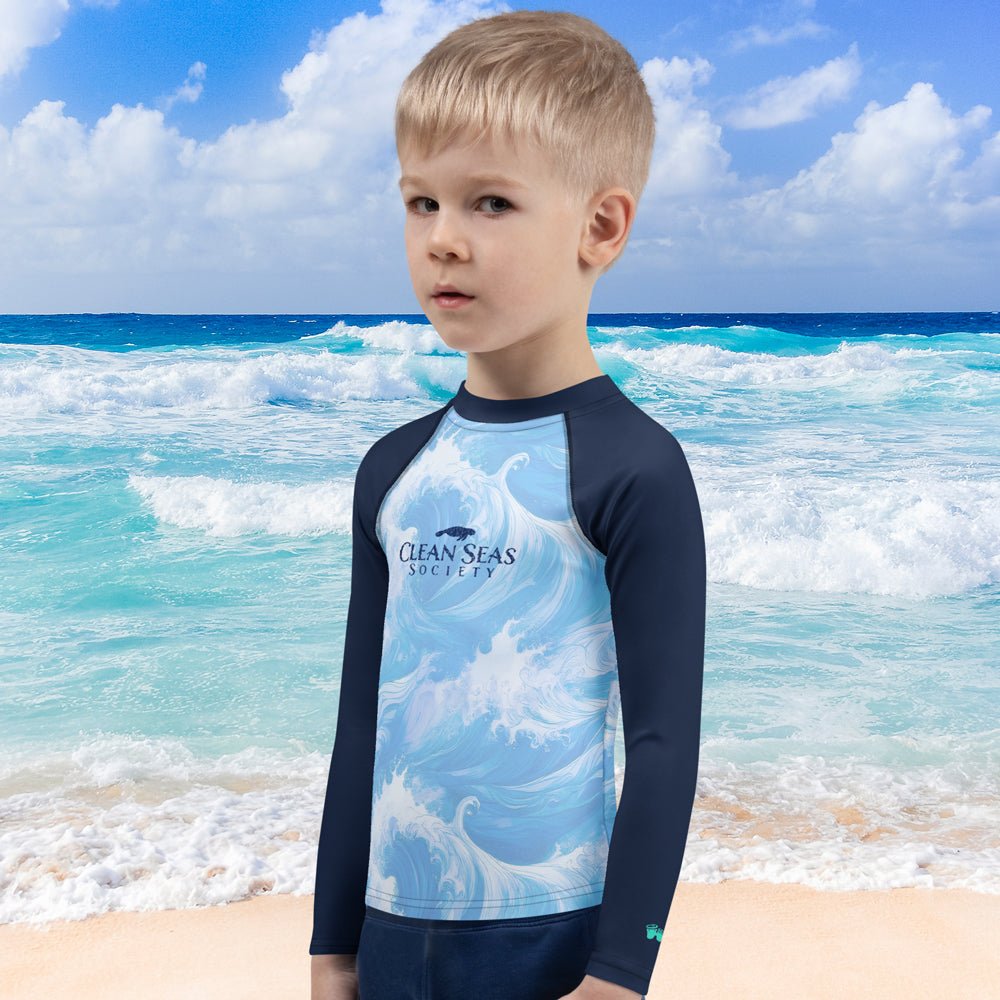 Child wearing a blue and navy rash guard with 'Clean Seas Society' logo on a beach.