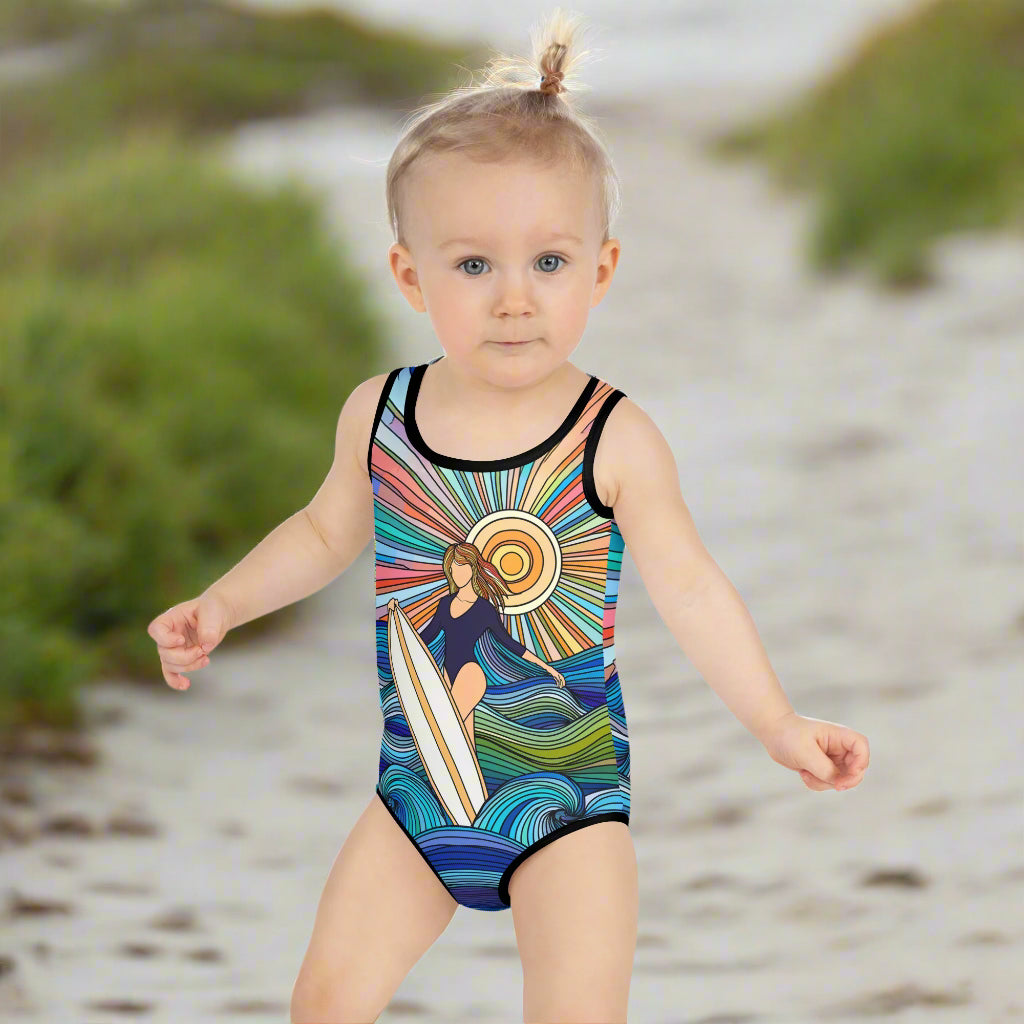 Girl's Surfer in the Sun one piece swimsuit worn by a toddler making her way down the beach