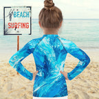 Person wearing a blue rash guard with ocean wave pattern on a beach.