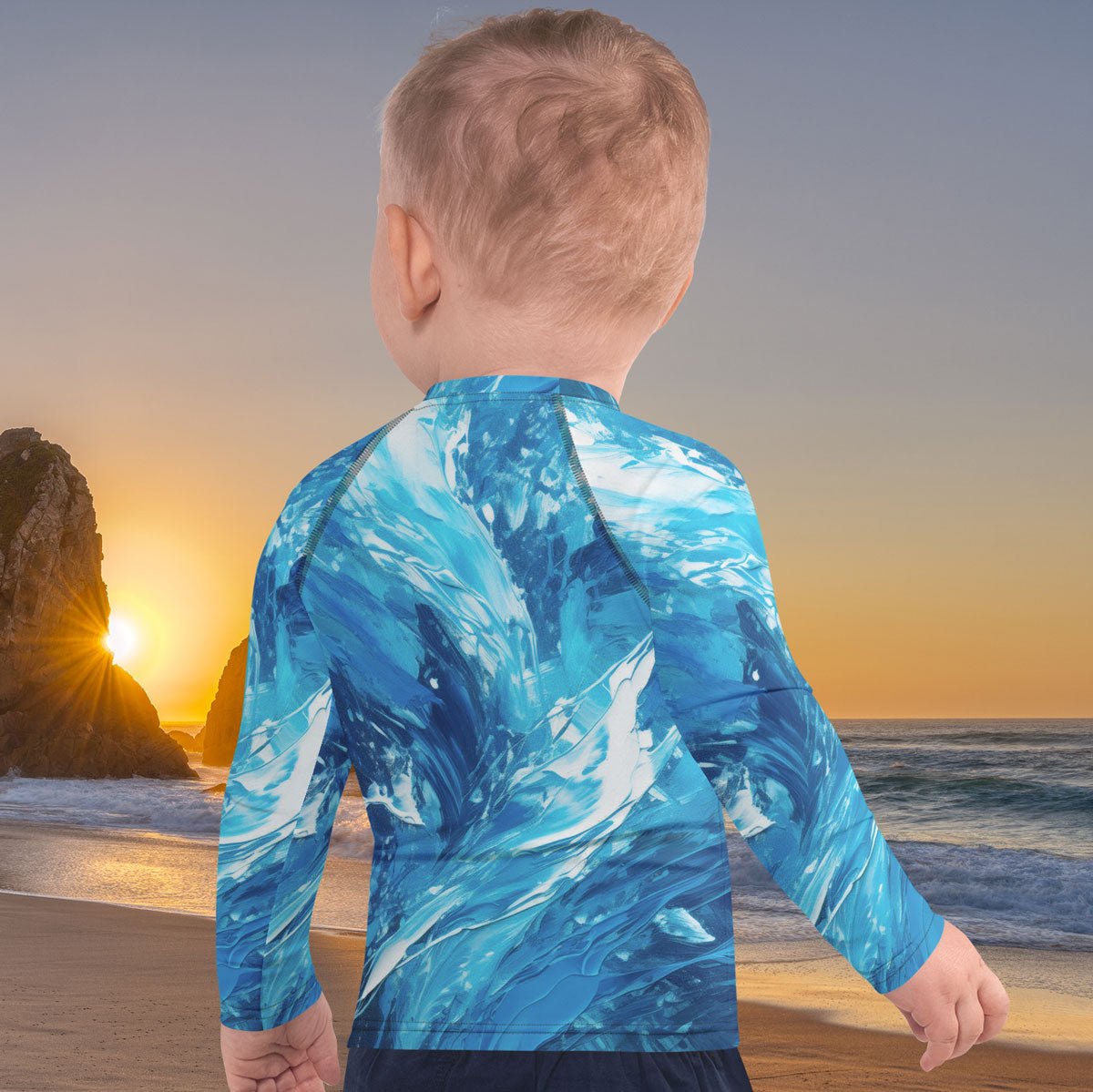 Child wearing a blue wave-patterned shirt standing on a beach with a sunset in the background
