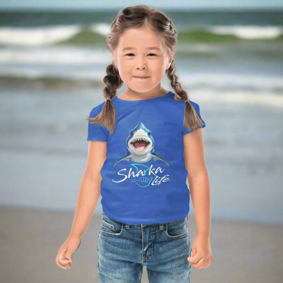 Cute Kid wearing a blue t-shirt with a shark graphic and 'Sharka' life' text hanging out on Daytona Beach