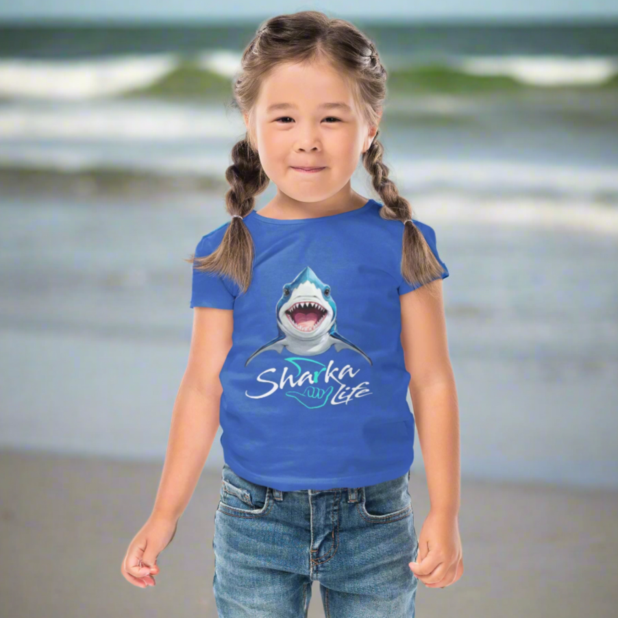 Cute Kid wearing a blue t-shirt with a shark graphic and 'Sharka' life' text hanging out on Daytona Beach