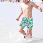 Child wearing palm tree patterned swim shorts playing in shallow water.