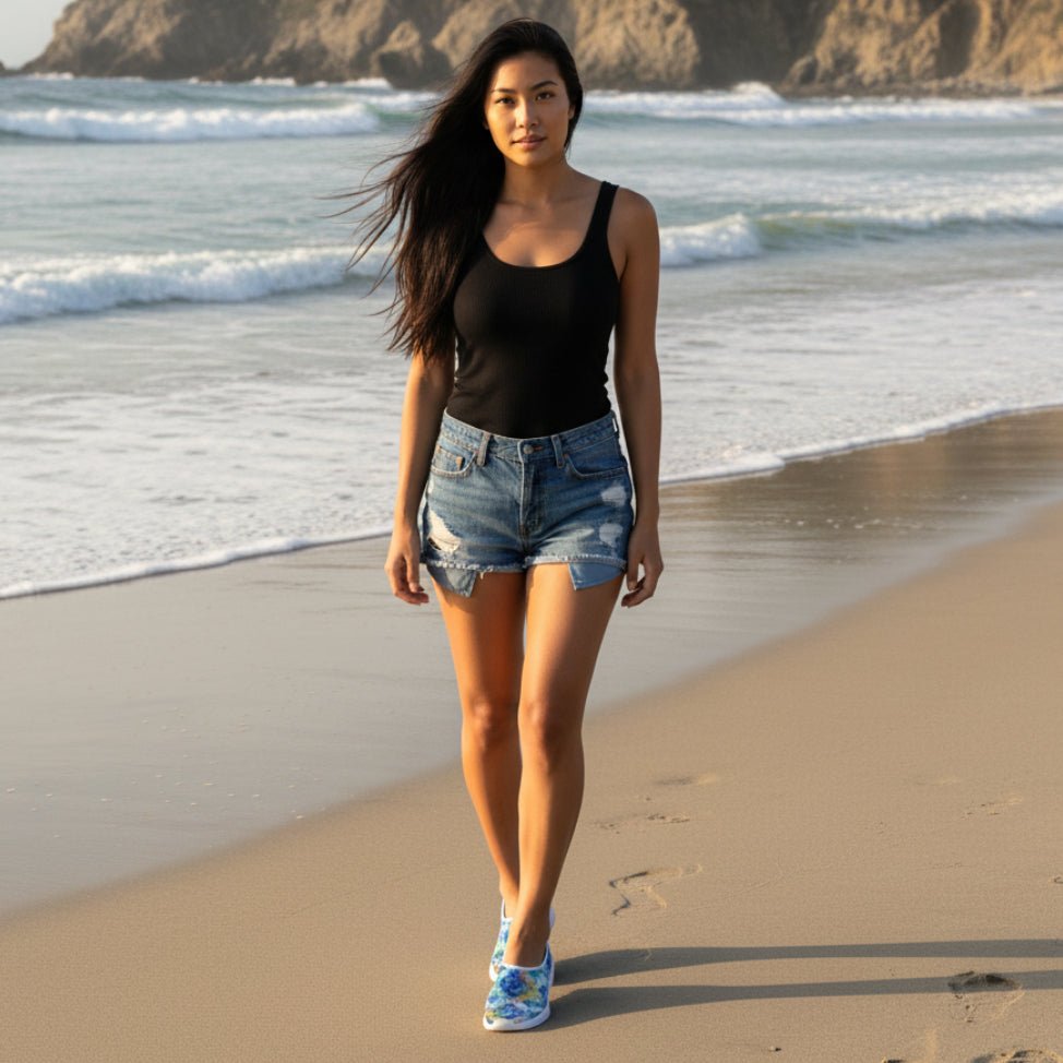 beautiful woman wearing tie dye beach slippers with blue jean shorts and a black tank top walking on Half Moon Bay State Beach in California
