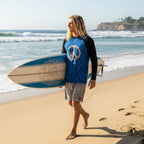 Surfer dude with long stringy blond hair holding a surfboard walking along Laguna Beach wearing a Seashell peace sign rash guard