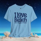 A light blue graphic t-shirt with the text 'I Love The Beach and 2 maybe 3 People' in dark navy blue, displayed on a beach scene background with sand, shells, and a starry night sky.