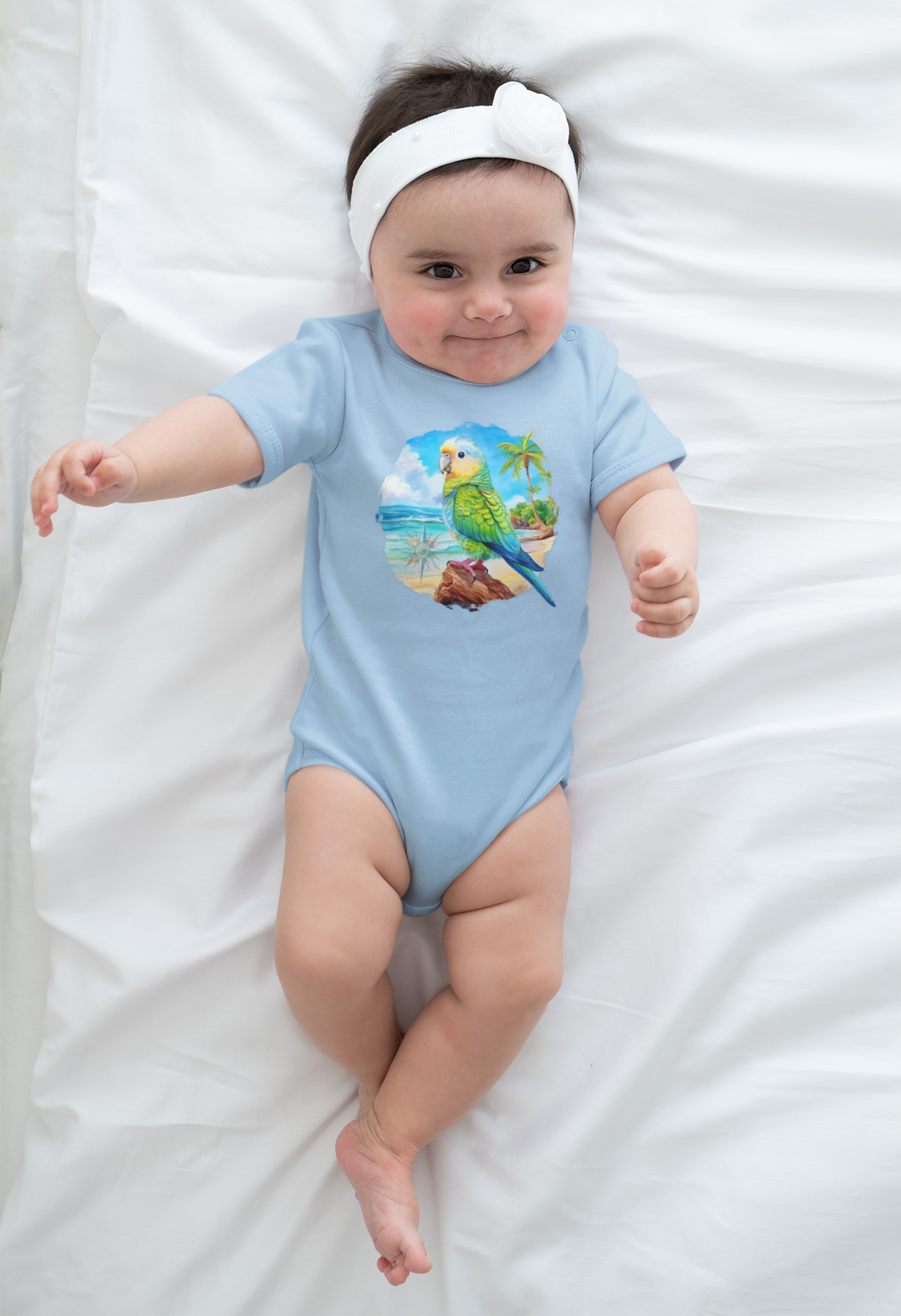 Baby wearing a light blue onesie with a parrot design on a white blanket