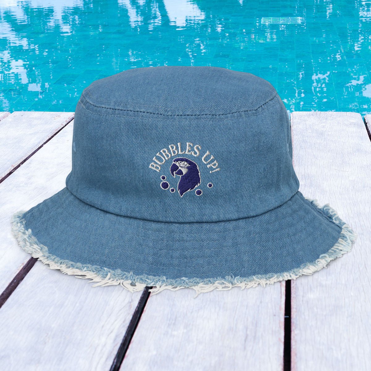 Blue bucket hat with 'Bubbles Up!' text and graphic on a wooden surface with blue water background