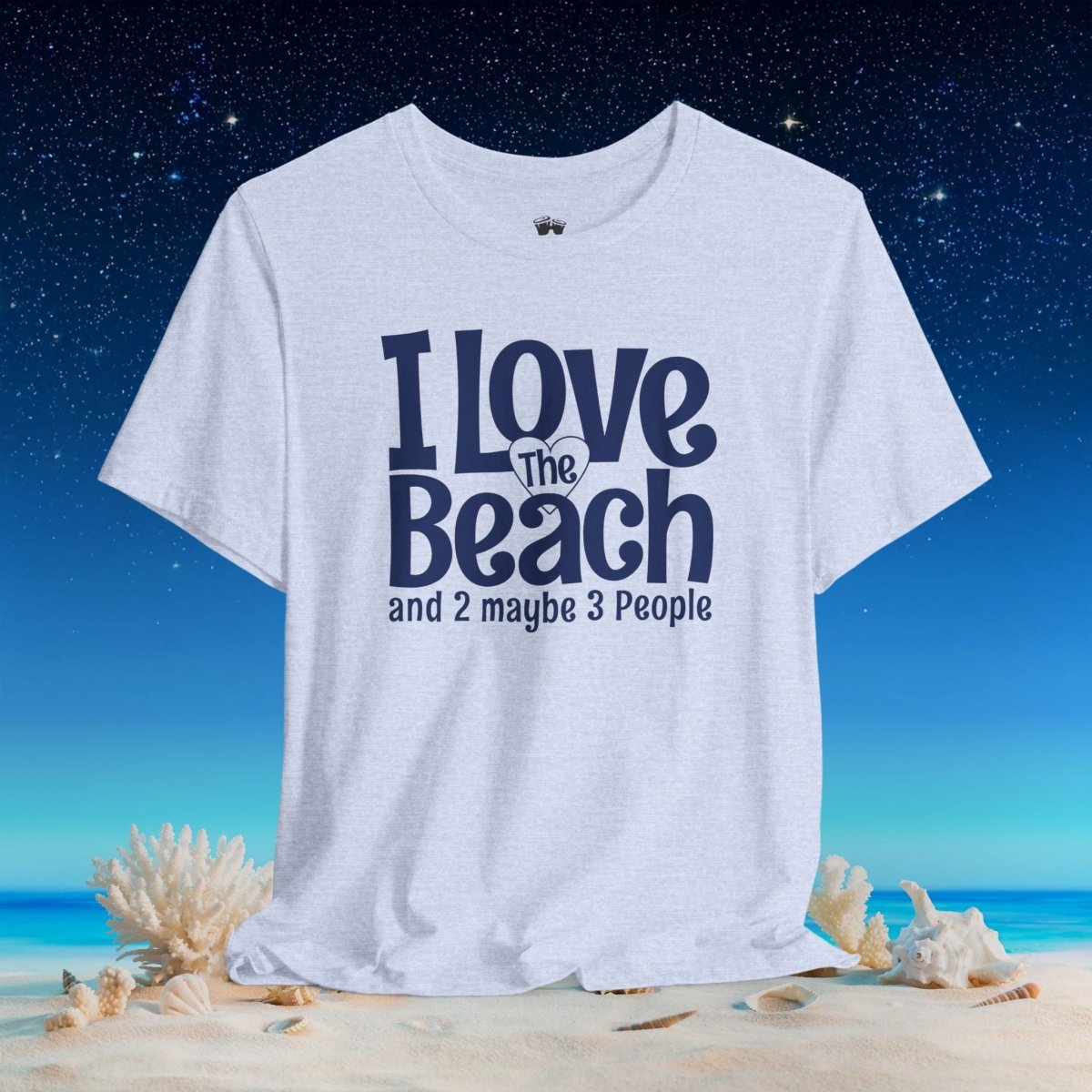 A light heather gray graphic t-shirt with the text 'I Love The Beach and 2 maybe 3 People' in navy blue, displayed on a beach scene background with sand, shells, and a starry night sky.