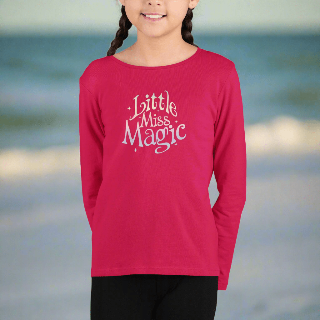 Girl wearing a red long-sleeve shirt with 'Little Miss Magic' text on the beach in St. Pete 