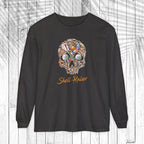 A black long-sleeve t-shirt with a colorful skull graphic made of various small objects and the text 'Shell-Raiser' in orange cursive, displayed on a white wood plank background.