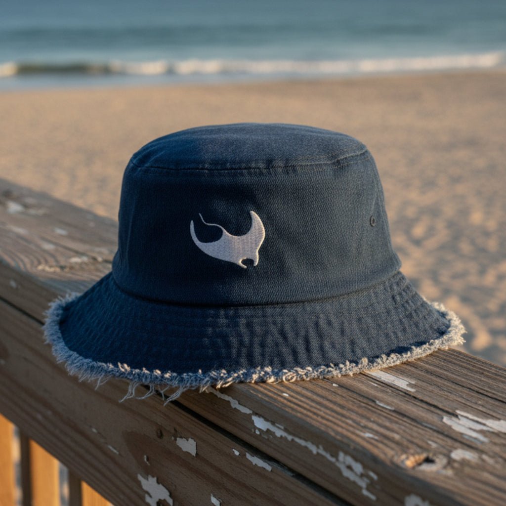 Navy blue bucket hat with a white manta ray embroidery on a beachside boardwalk