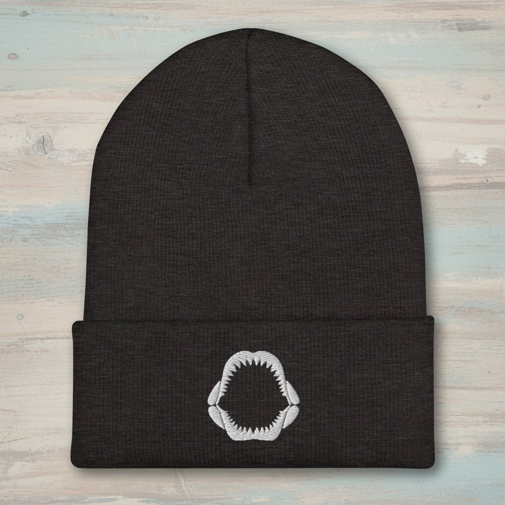 Black beanie with a white megalodon jaw embroidery on a faded wood background